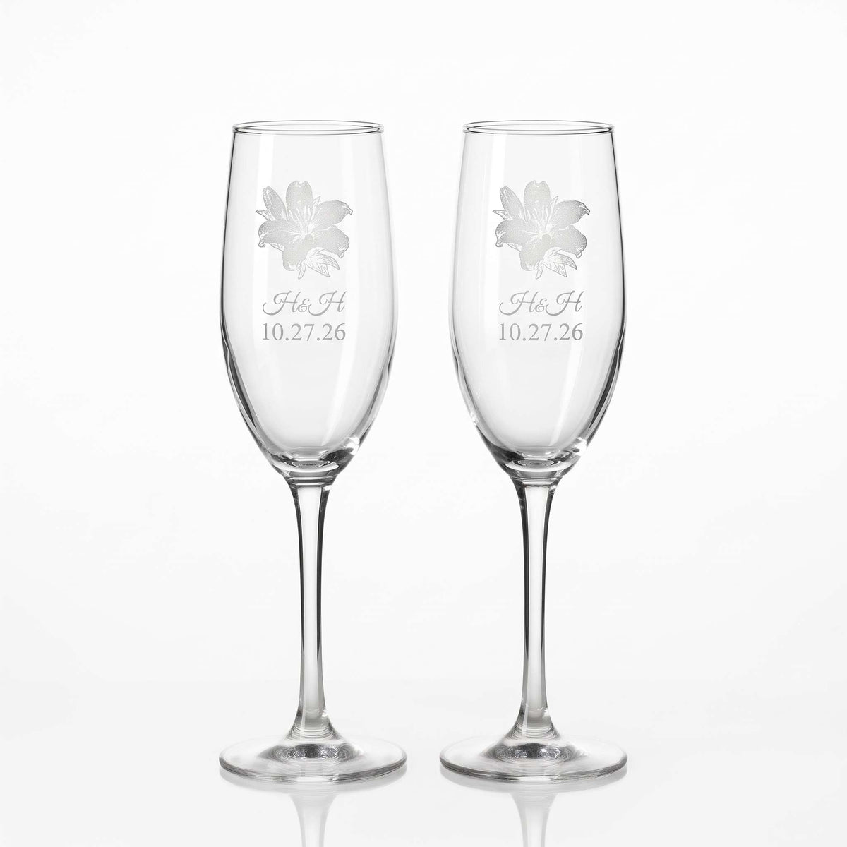 Two glass champagne flutes custom engraved for wedding. Engraved flower, initials of bride and groom, and the date of their wedding.