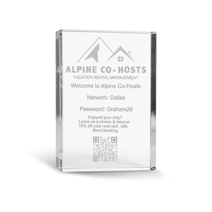 A clear acrylic or glass plaque displaying personalized vacation rental information for Alpine Co-Hosts, including a welcome message, network location, password, review request, and a QR code, shown on a white background.