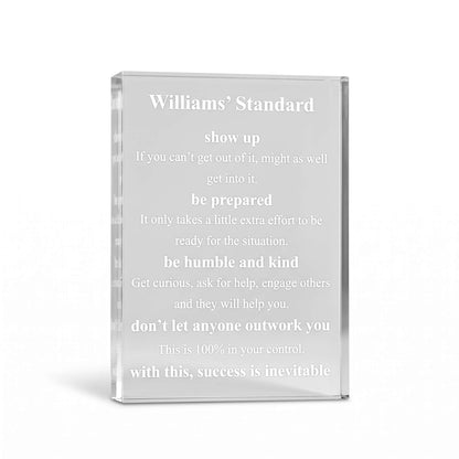 A clear acrylic or glass standee with engraved white text reading 'Williams' Standard' and a motivational quote, shown on a clean white background.