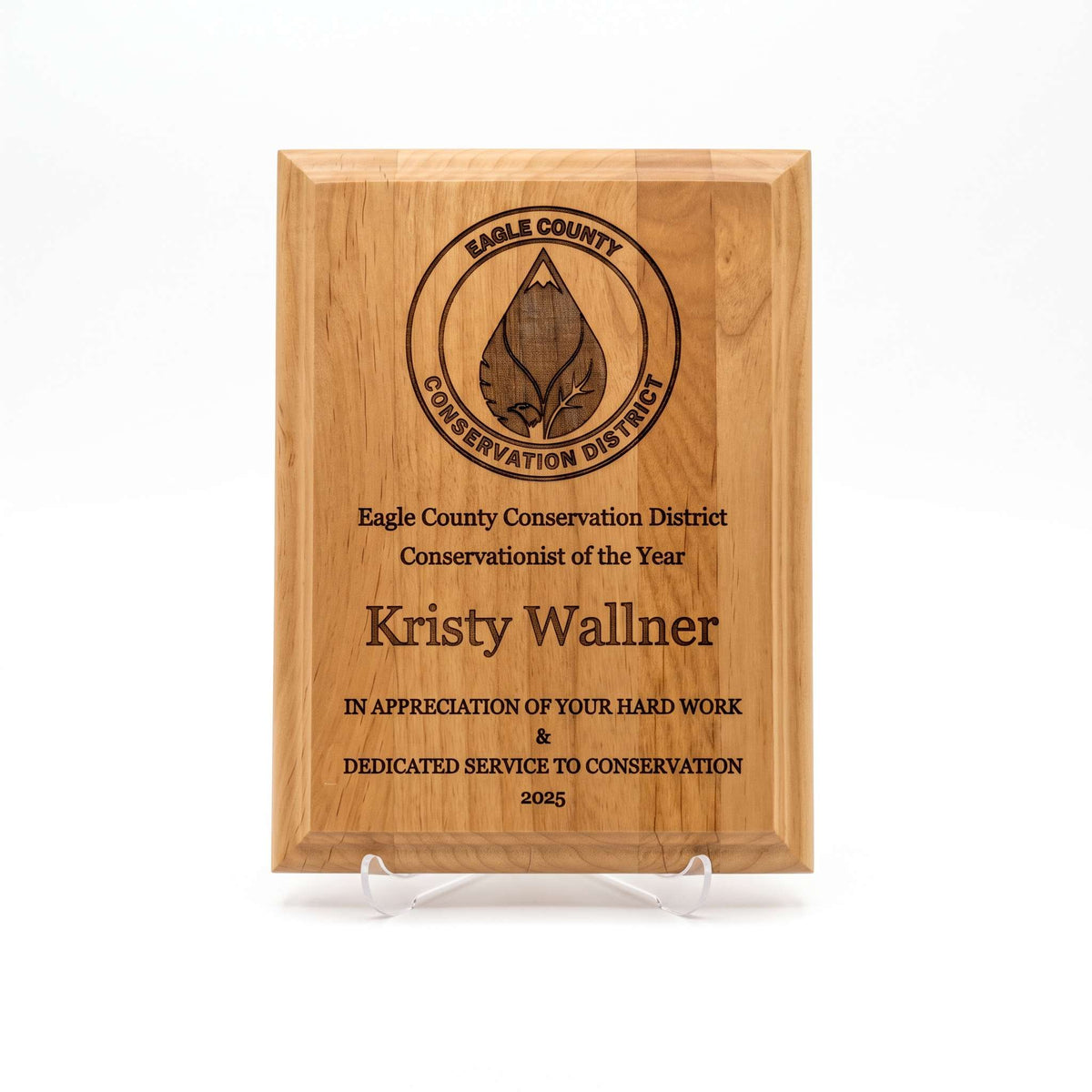 A rectangular wooden plaque on a clear display stand, engraved with the Eagle County Conservation District logo and the name Kristy Wallner, Conservationist of the Year. Photographed on a white background.