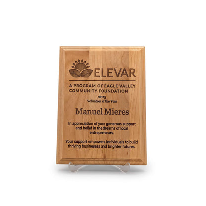 A personalized wooden plaque on a clear acrylic stand, engraved with the text 'ELEVAR A PROGRAM OF EAGLE VALLEY COMMUNITY FOUNDATION 2025 Volunteer of the Year Manuel Mieres' In Appreciation for his generous support. on a white background.