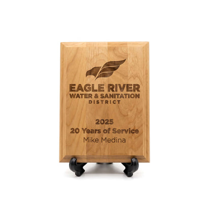 A rectangular wooden plaque on a small black display stand, engraved with the Eagle River Water & Sanitation District logo and the text '2025 20 Years of Service Mike Medina' on a white background.