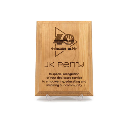 A personalized wooden plaque on a clear acrylic display stand, featuring a custom engraved logo and text for 'JK Perry'  in recognition of his service and impact on community. on a clean white background.