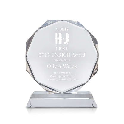 A faceted clear crystal award plaque on a rectangular base, engraved with the text '2025 ENRICH Award presented to Olivia Weick' and a logo, shown on a white background.