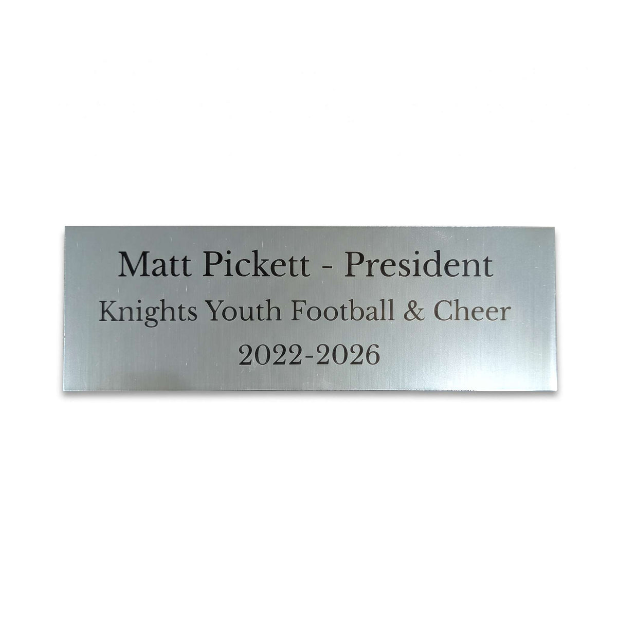 A rectangular brushed silver metal name plaque with black engraved text reading 'Matt Pickett - President', 'Knights Youth Football & Cheer', and '2022-2026' on a plain white background.